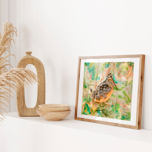Framed artwork of a woodcock bird on a white surface with decorative items.