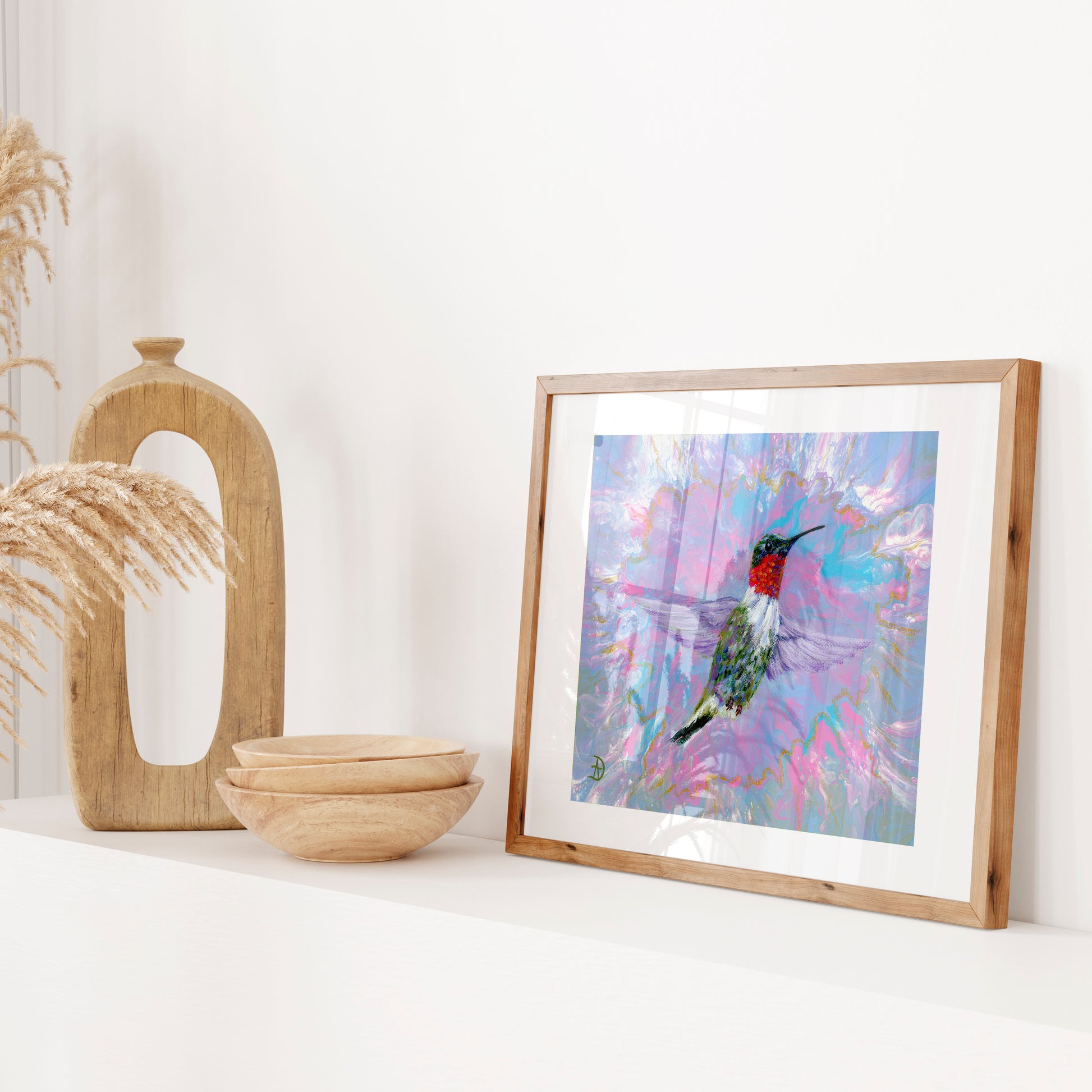 Framed artwork of a hummingbird on a white surface with decorative items.