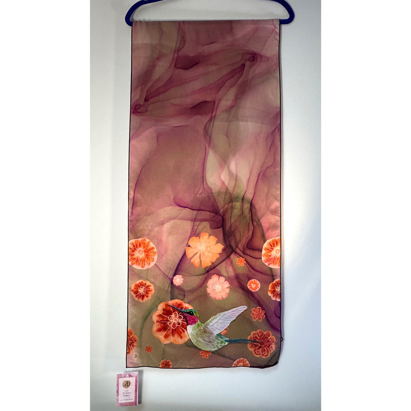 Decorative silk scarf with floral and hummingbird design on a hanger against a white background. Unique silk scarf suitable for client appreciation gifts and luxury corporate gifts. 