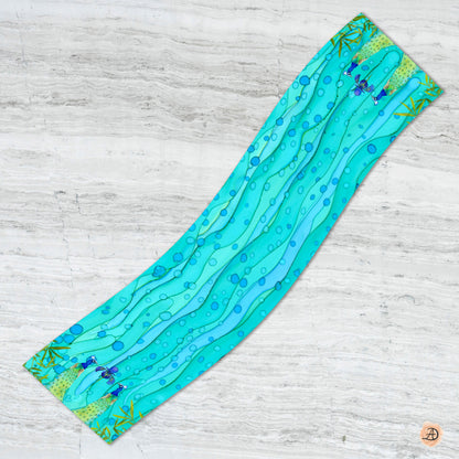 Teal silk scarf with wave pattern and peacocks on a light wooden surface. Unique silk scarf suitable for client appreciation gifts and luxury corporate gifts. 