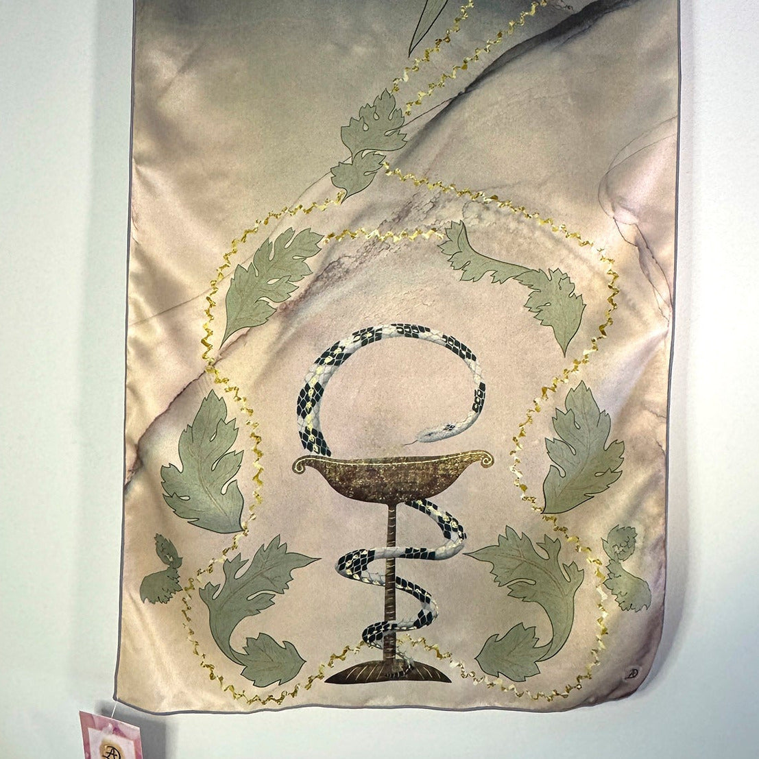 Decorative silk scarf with a snake around a chalice design, surrounded by acanthus leaves on a tan and sage green background.